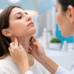 KBB uzmanı doktor, kadın hastanın çene altı lenf bezlerini ve boyun bölgesini eliyle muayene ediyor.
