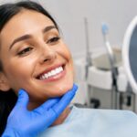 Diş kliniğinde elinde ayna tutarak Hollywood gülüşü (Hollywood smile) estetiği sonrası yeni ve beyaz dişlerine bakarak gülümseyen kadın hasta.